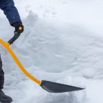 A man cleans snow in the yard with a shovel after a heavy snowfall.